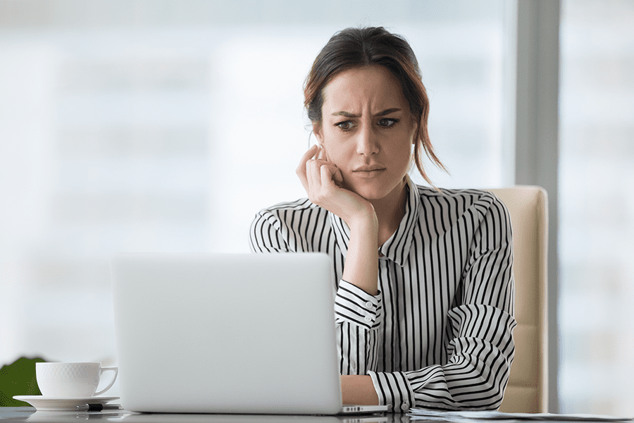 A woman in a striped shirt looks concerned while using her laptop to search for personal information online, with a cup and saucer on the desk beside her.