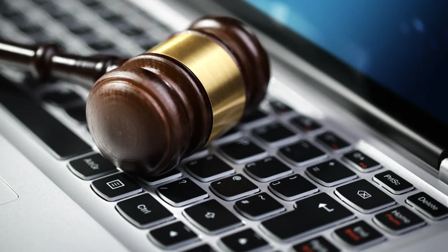 A wooden judge’s gavel with a brass band rests on the keyboard of a laptop computer, symbolizing the intersection of law and technology or online legal proceedings.